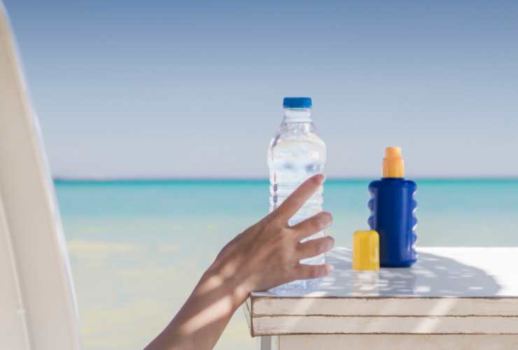 mano di donna che afferra bottiglietta d'acqua in spiaggia