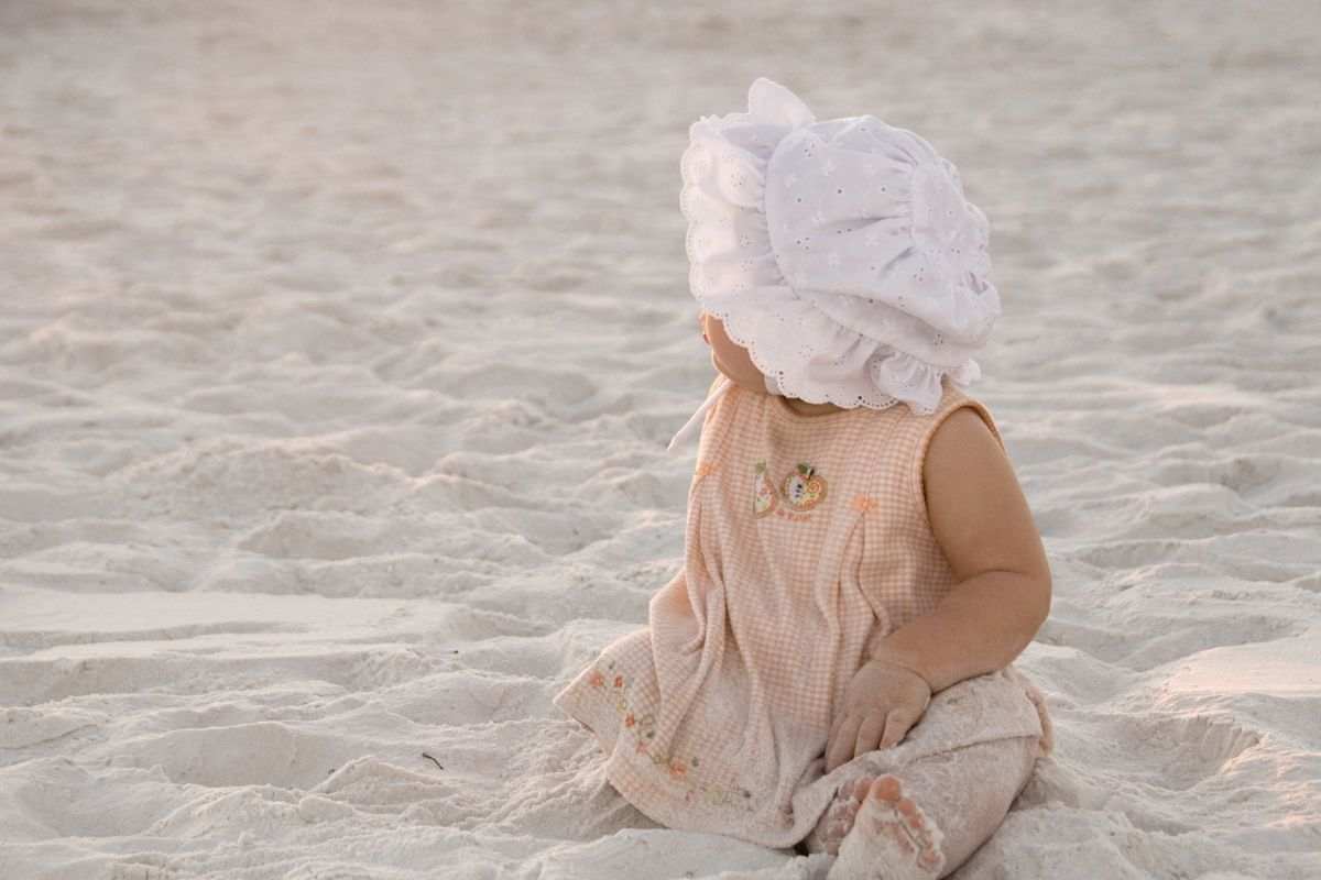 Bambina seduta sulla spiaggia com cappellino